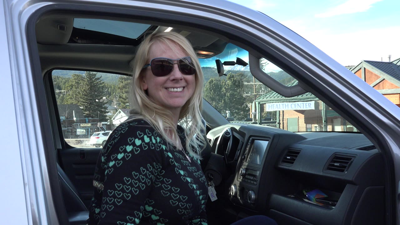 Blonde woman in sunglasses smiles from an open truck cab.