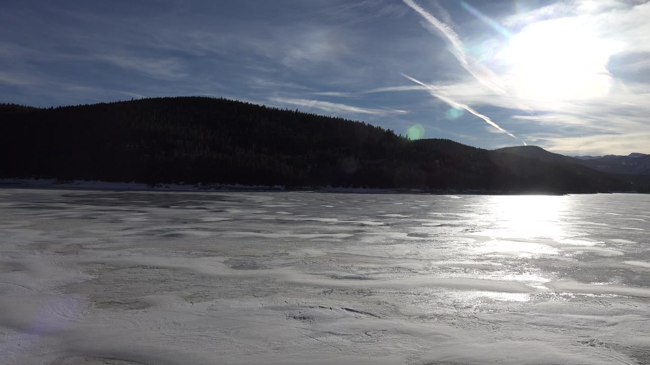 Second frame shows Nederland, Colorado lake ice with the sun blown out near the upper right, a dark tree-covered ridge, distant mountains, and no visible people.
