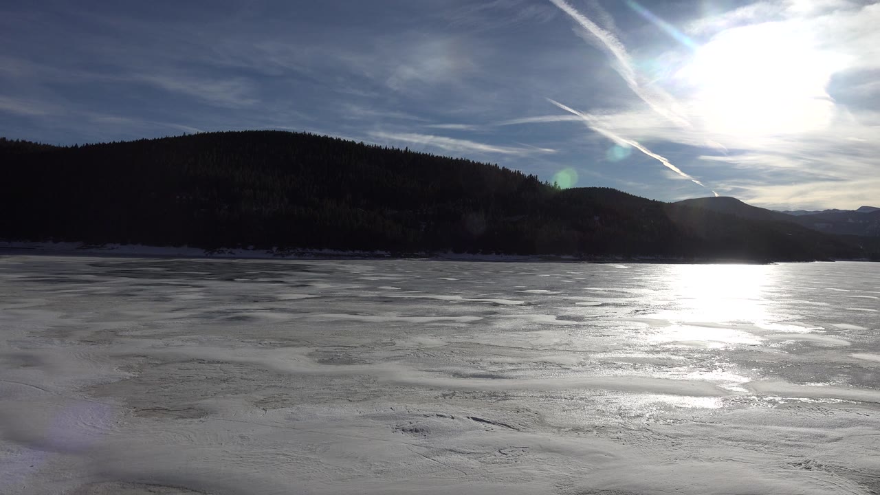Icy lake foreground with sun glare and shadowed hills.