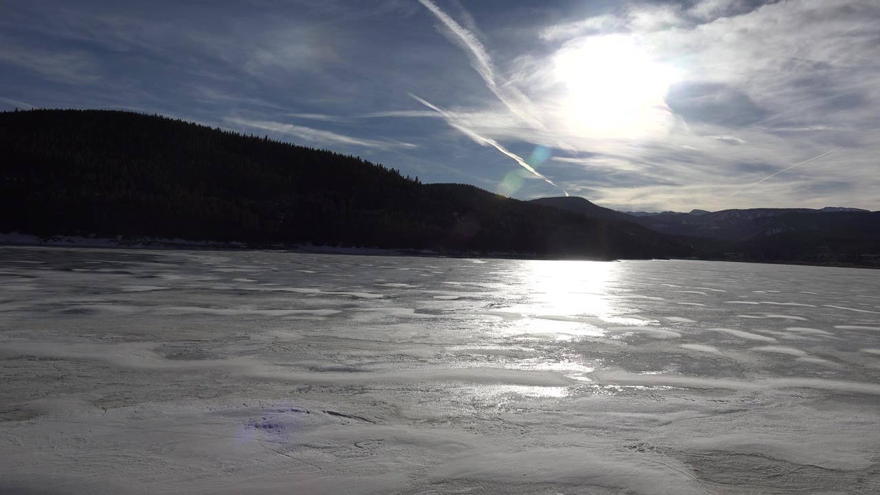 Frozen lake surface beneath streaked clouds and mountains
