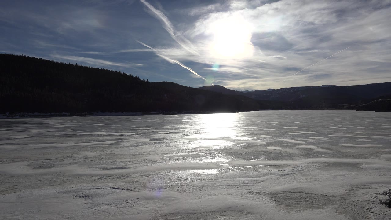 Frozen lake and wooded ridge beneath a cloudy winter sky.