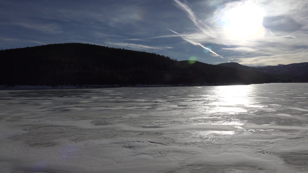 Foamy water reflects the sun below a cloudy blue sky and hills.
