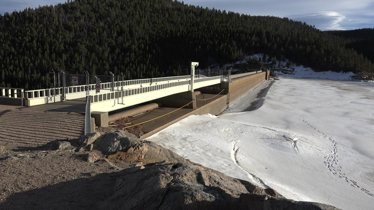 Snowy bridge beside frozen water and forested hills
