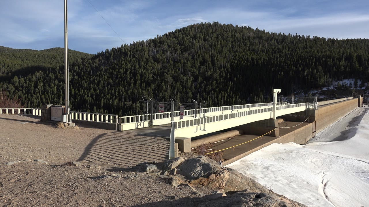 Sunlit bridge railing with snow and wooded mountain