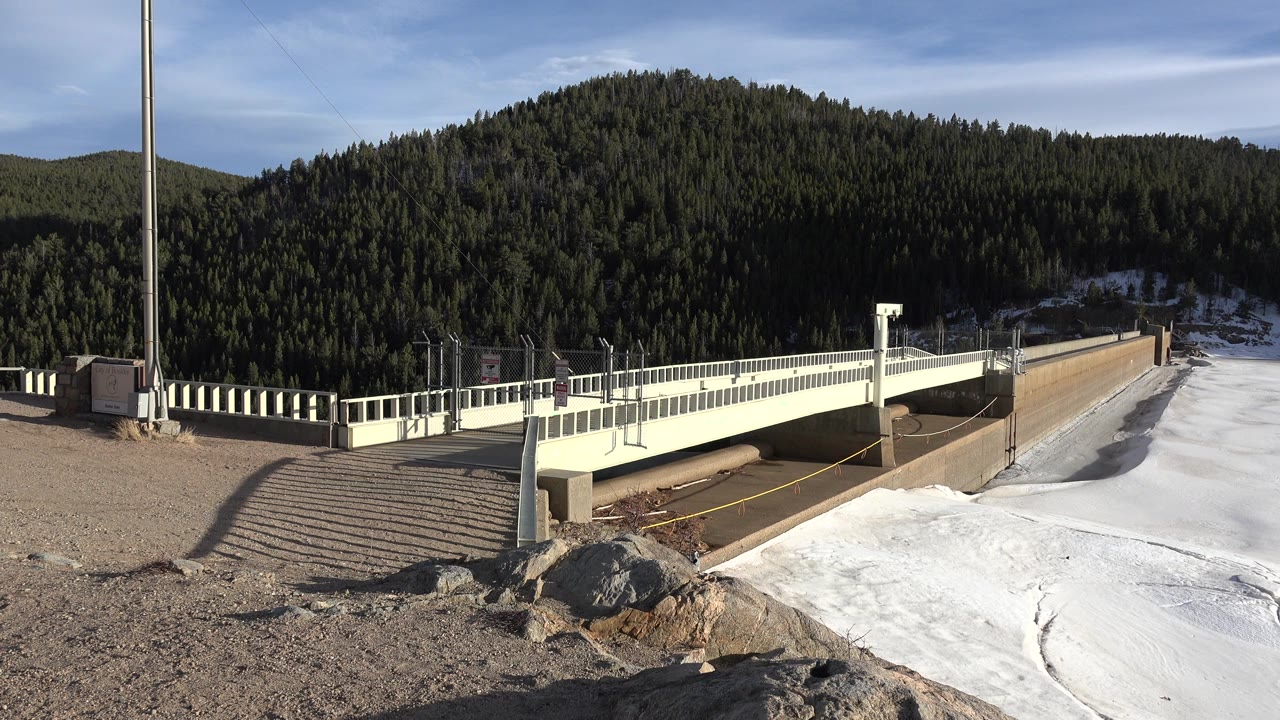 Bridge beside snow with evergreen mountain in background.