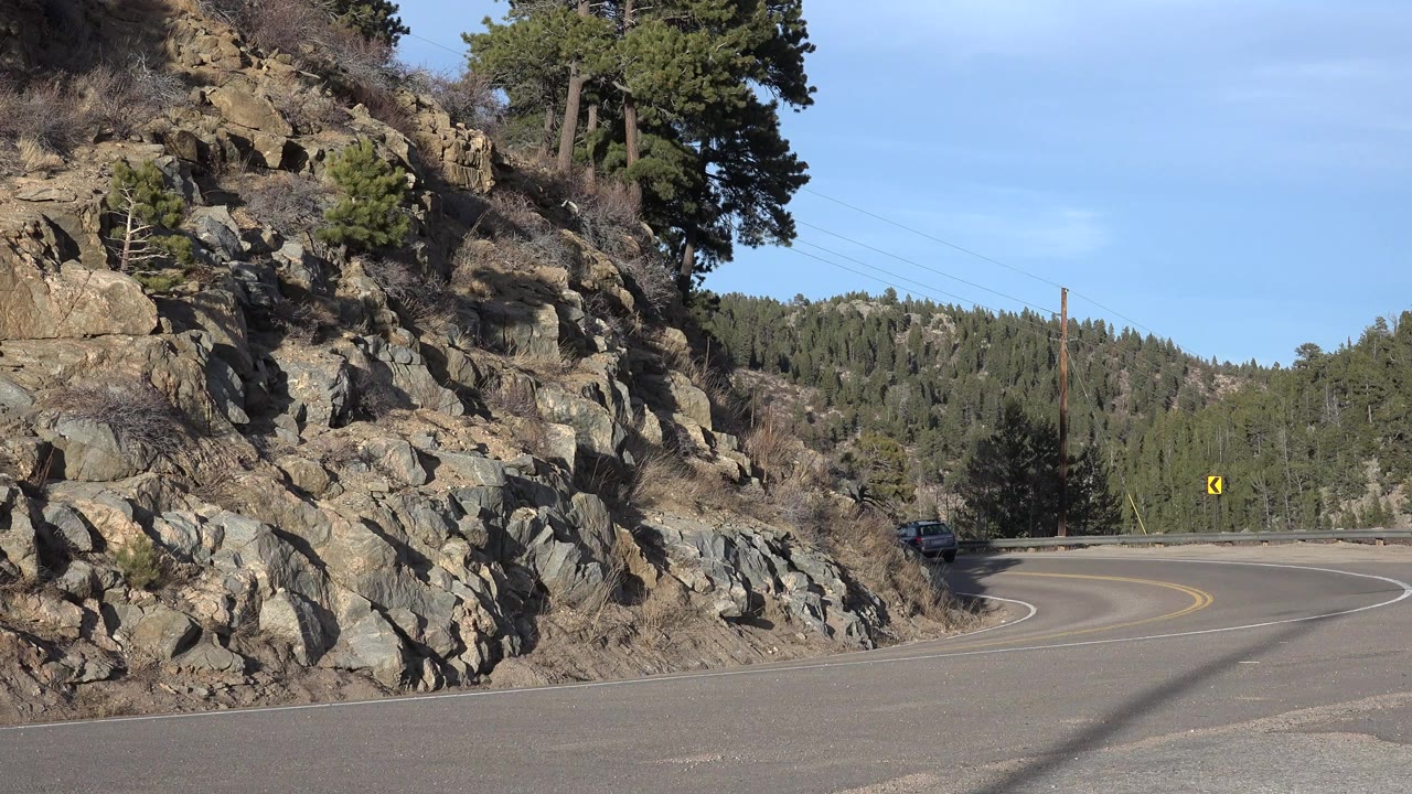 Curving mountain road beside a rocky hillside and pine trees