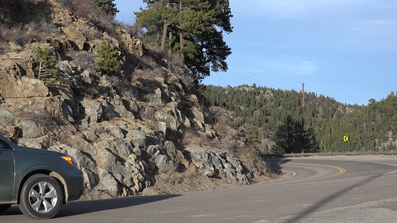 Front of a dark SUV entering a mountain road frame beside rocks.