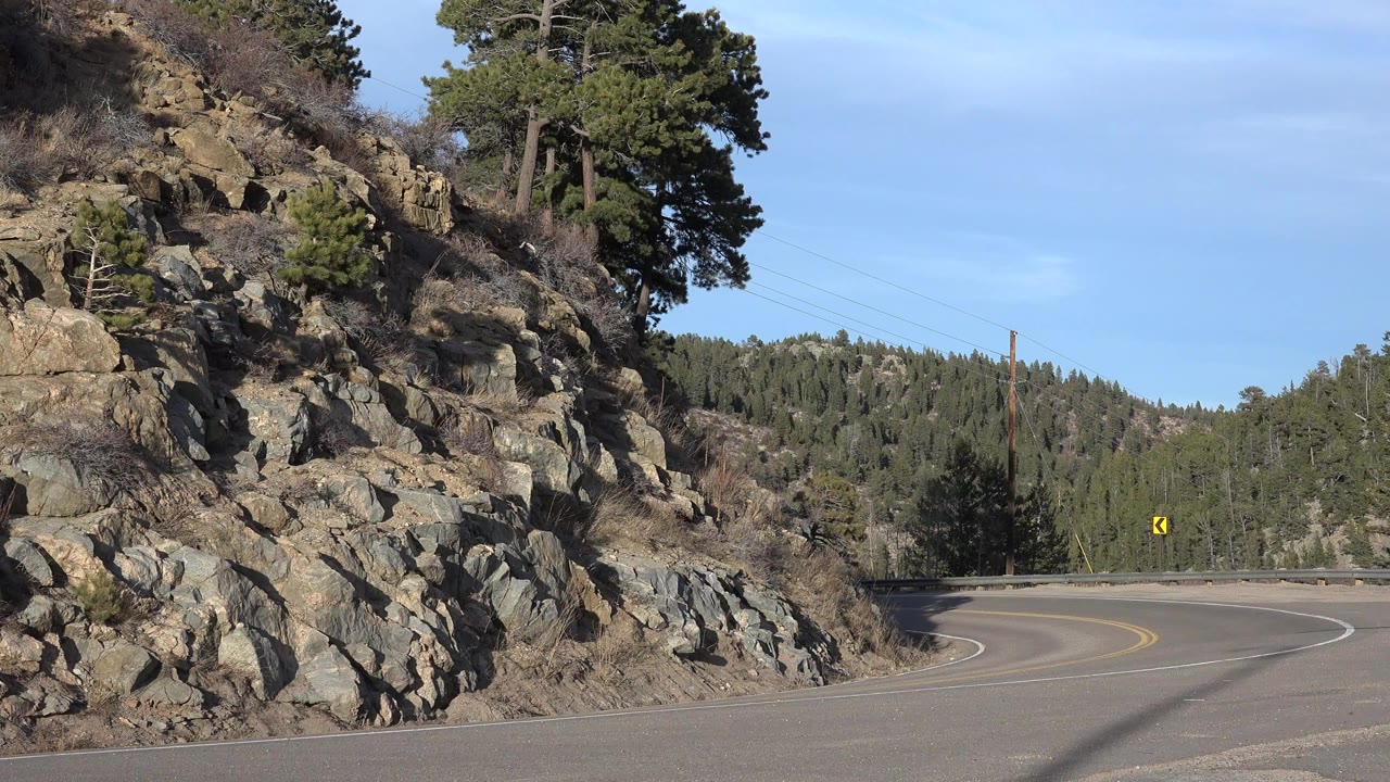 Empty mountain road curving left beside a rocky hillside
