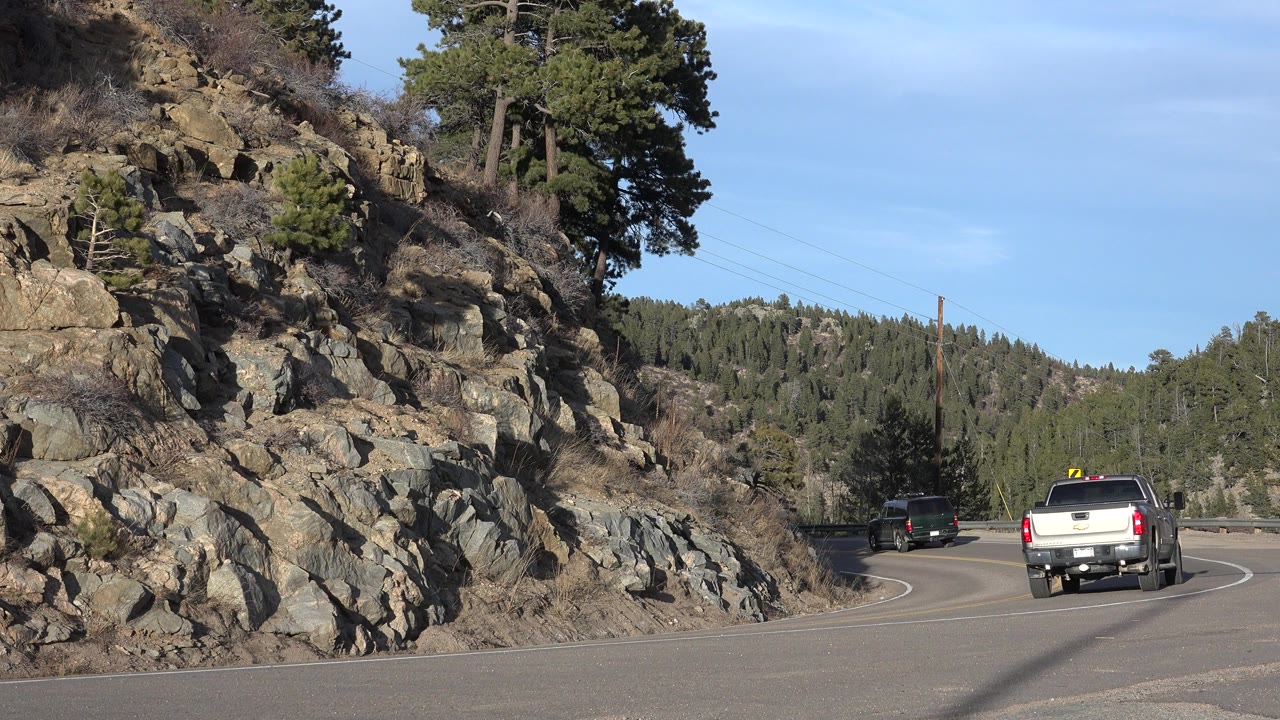 White pickup and dark SUV on a curving mountain road beside gray rocks.