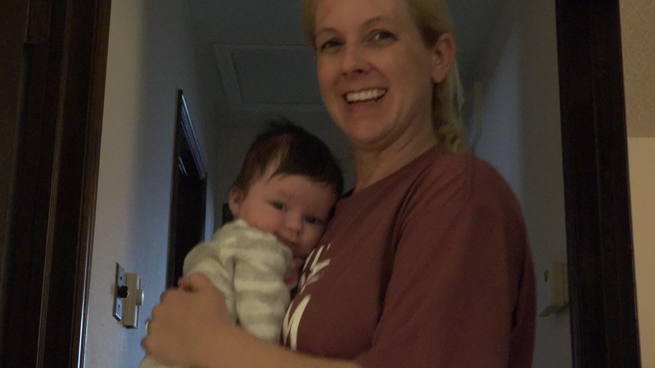In Westminster, Colorado, the woman remains smiling as the baby rests against her chest, with the doorway and dim hallway background still visible.