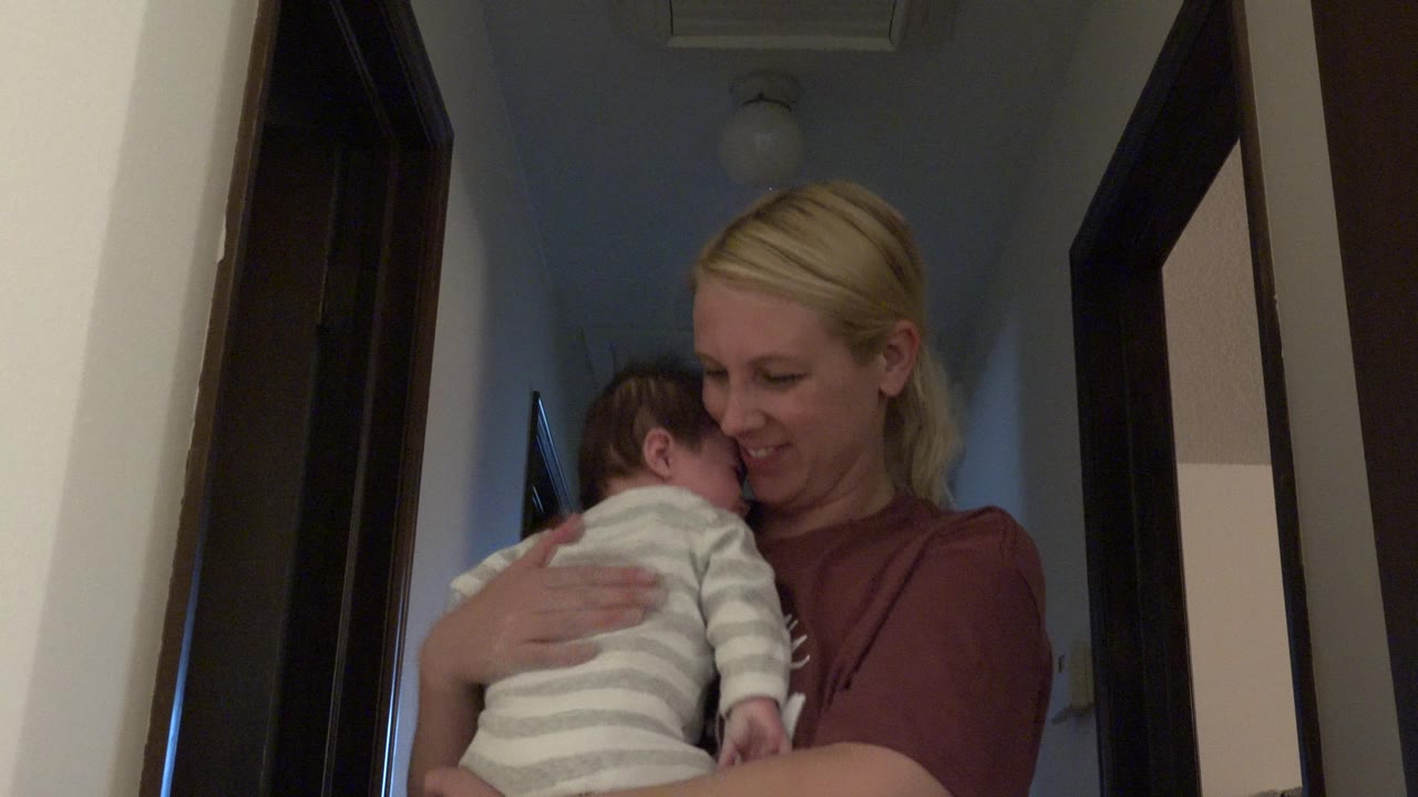 Mother holds a baby against her shoulder in a hallway.