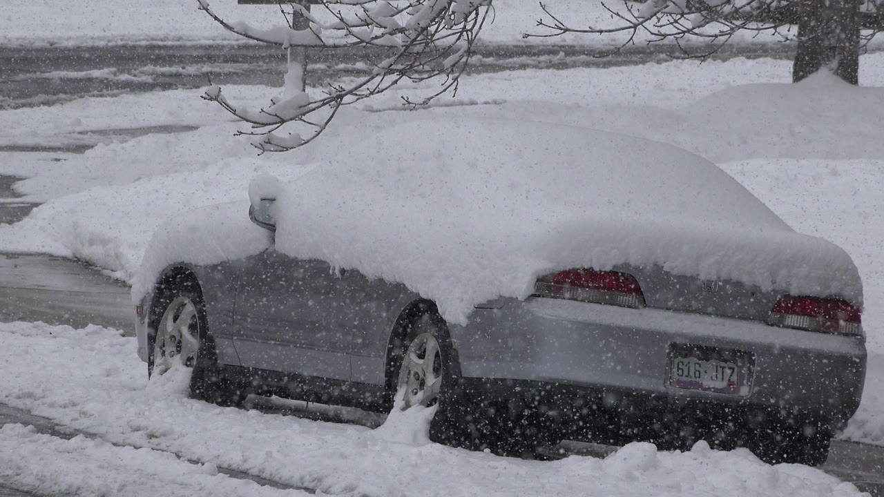 Gray car buried under snow beside a street.