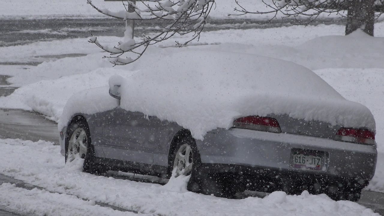Silver sedan buried in snow beside a slushy street.
