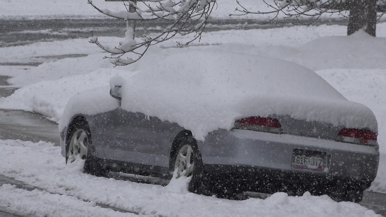 Snow-covered gray car parked beside a slushy road.