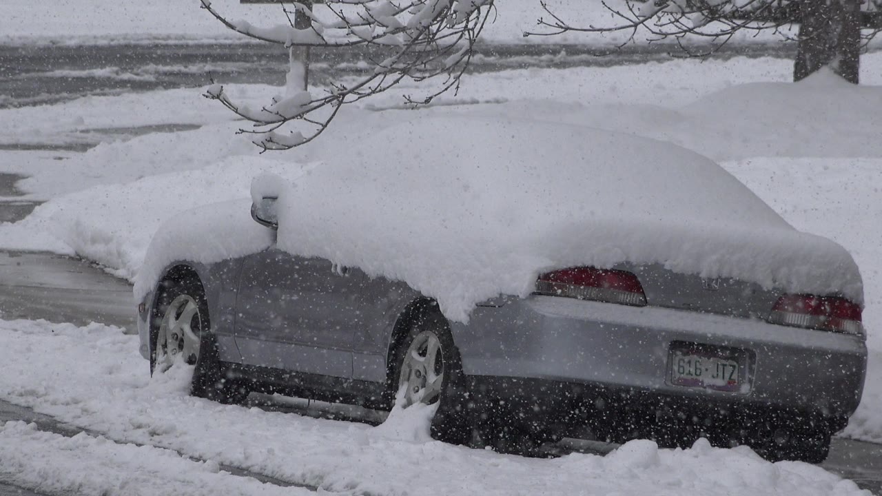 Snow-covered gray sedan parked beside a snowy road