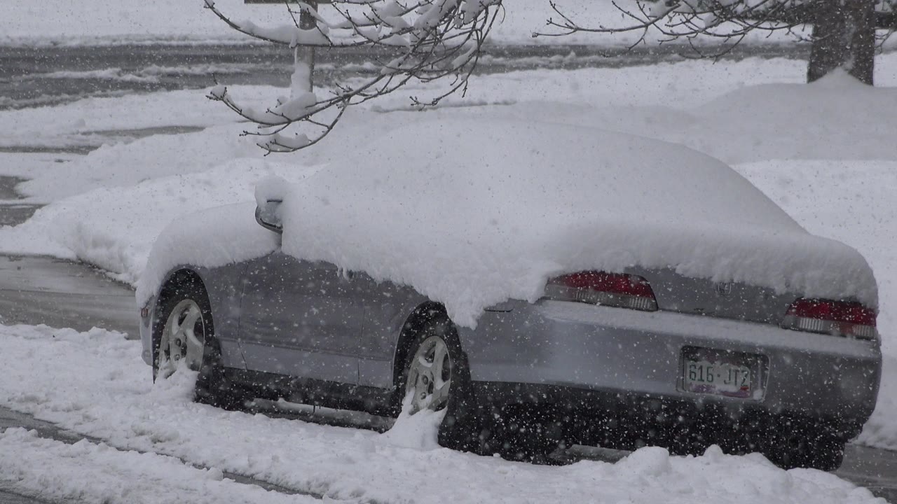 The parked sedan remains framed from the rear side in Westminster, Colorado, with deep snow on the roof, trunk, and ground, and no visible people.
