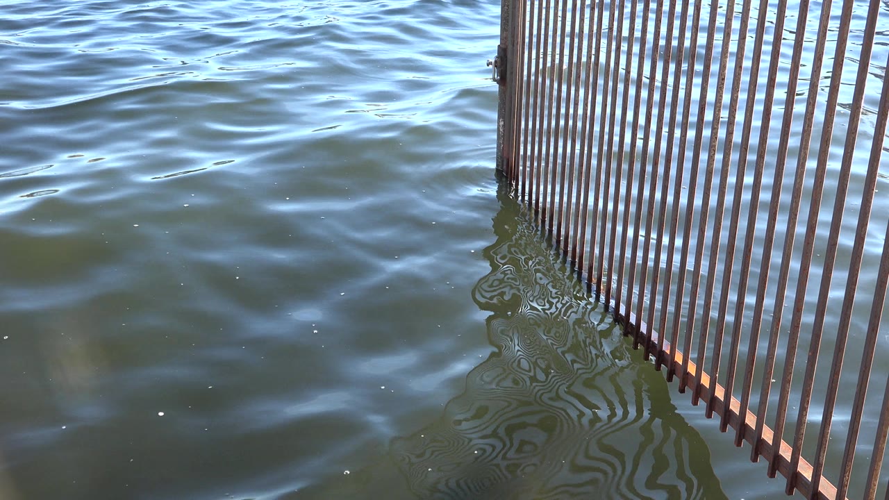 Rippling water in Westminster, Colorado surrounds the lower edge of the slatted structure, with bright reflections across the surface and no visible people.