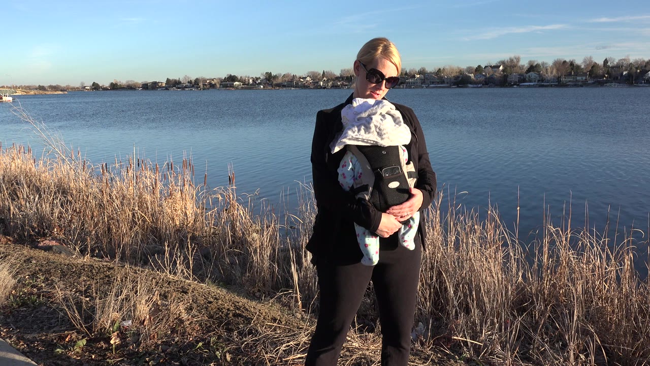 Woman in sunglasses holding a baby beside a lake.