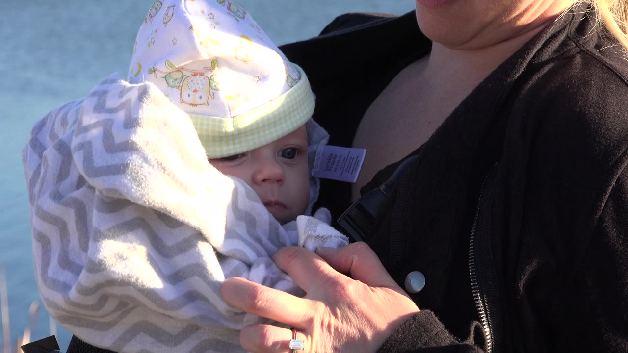In Westminster, Colorado, a woman in a dark jacket holds a baby wrapped in a gray patterned blanket, with the baby's face partly visible under a pale cap.