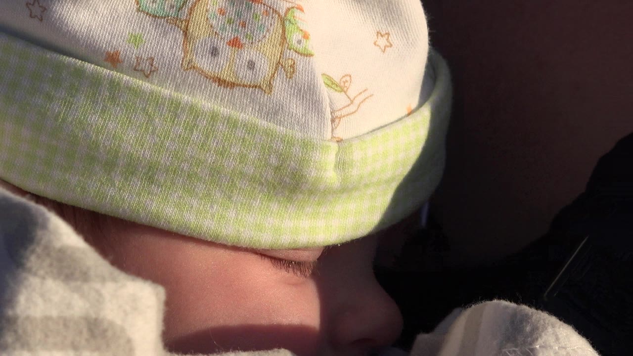 Close-up of a bundled baby in Westminster, Colorado, with a patterned knit hat pulled low and warm sunlight crossing the face and blanket.
