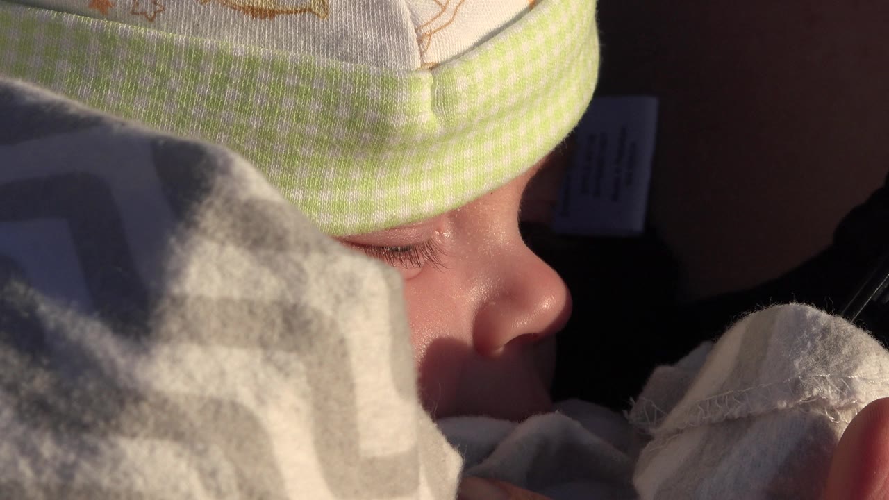 Profile close-up of a bundled baby with a hand near the blanket.