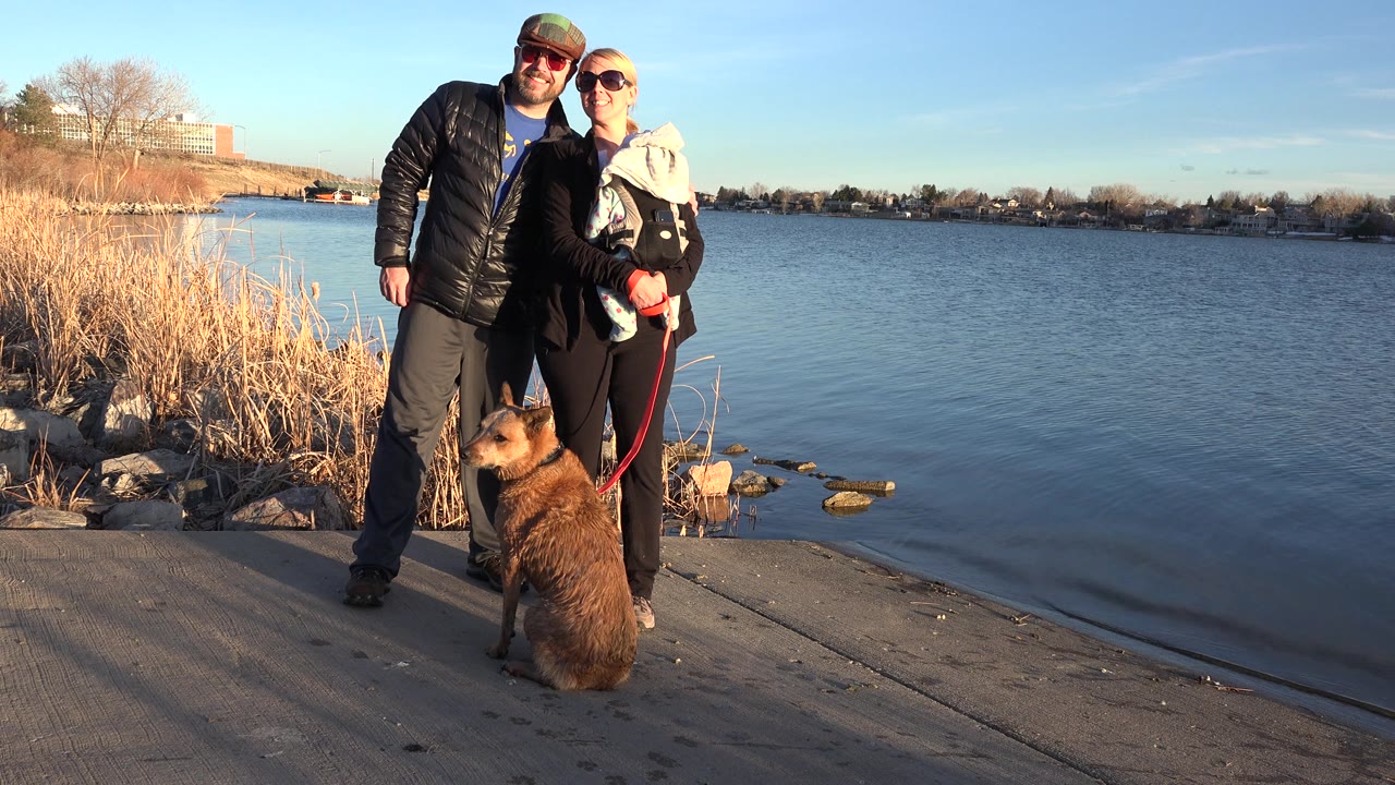 Adults with baby and dog on leash near lake.