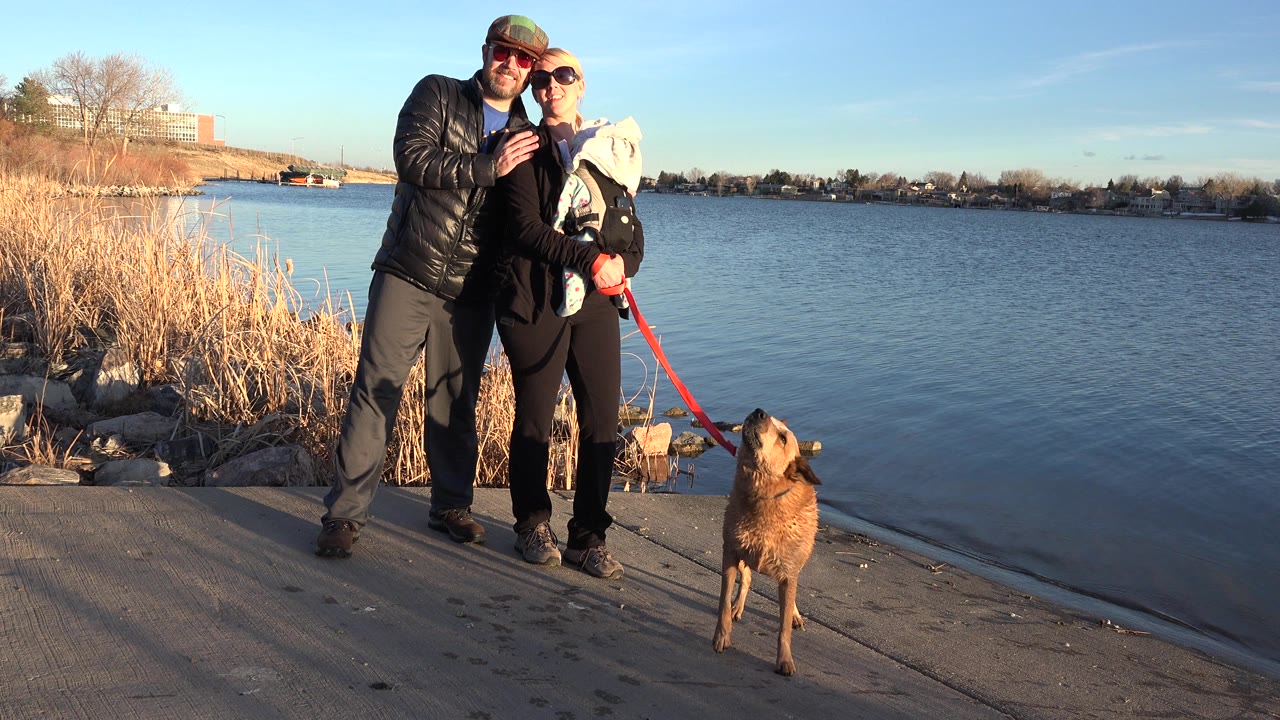 Couple posing with a brown dog by a lake.