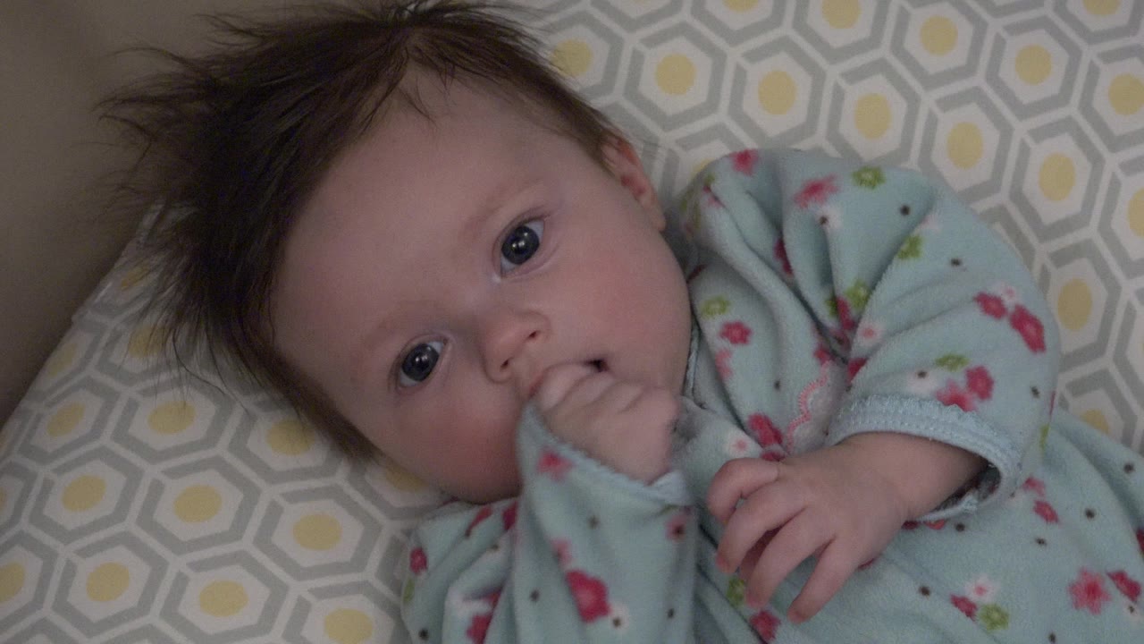 In Westminster, Colorado, the baby looks toward the camera with the left hand at the mouth and the other hand resting across the sleeper.