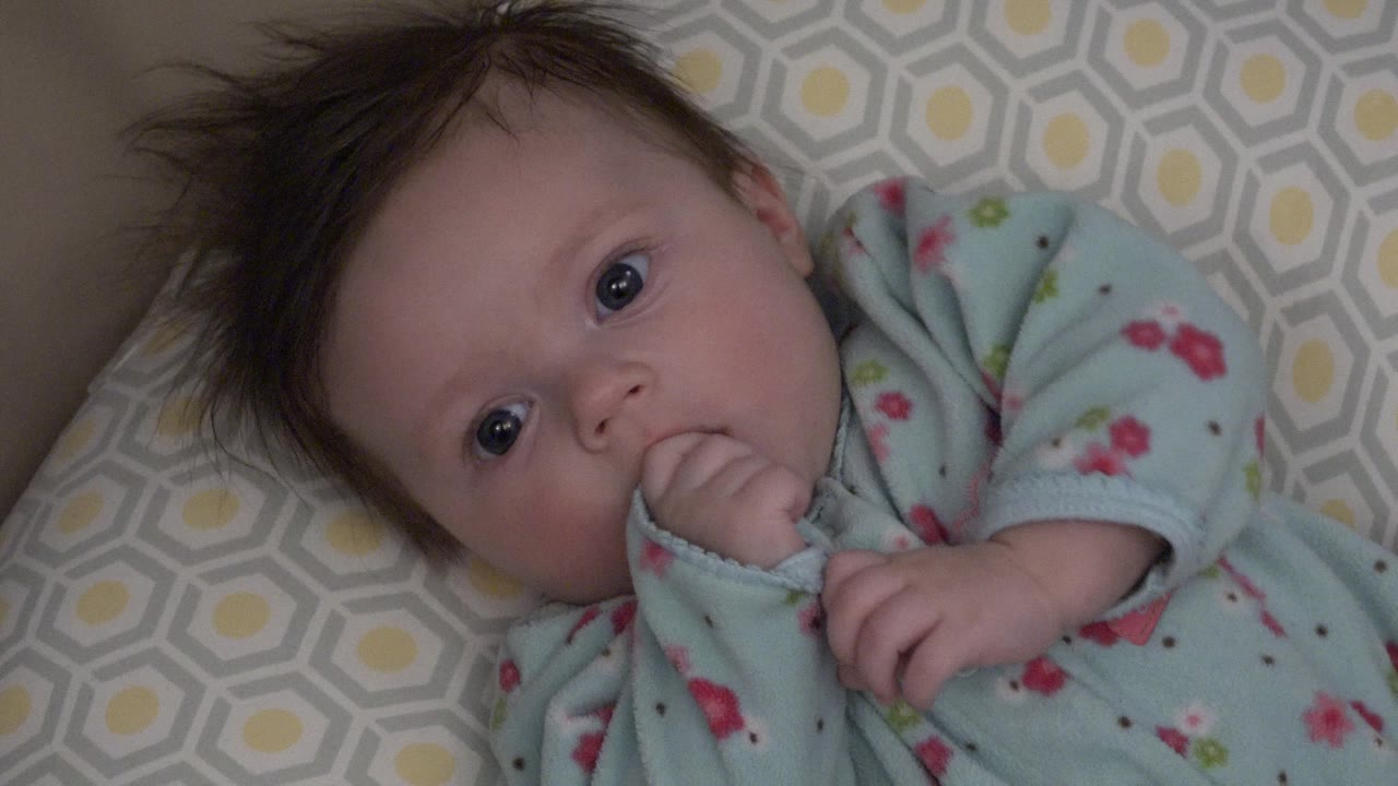 Baby lying close to camera with hand in mouth.