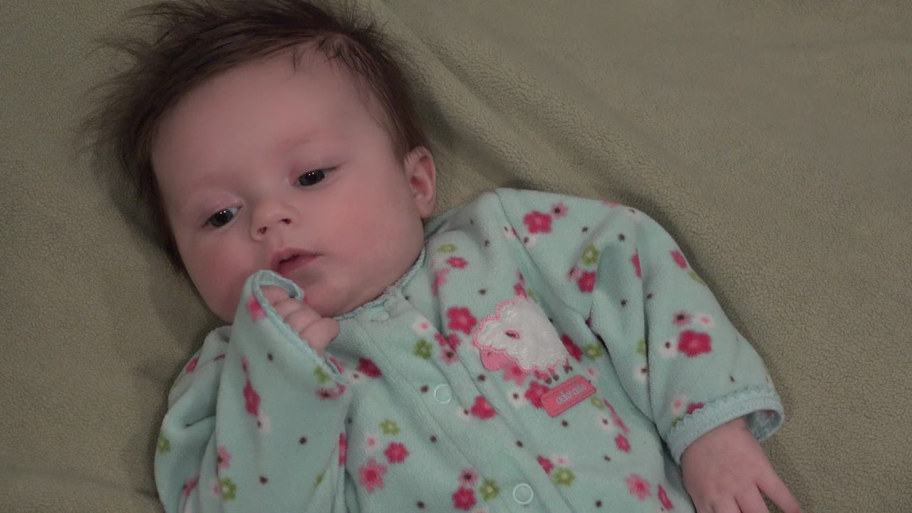 White baby lying on an olive blanket in a mint floral sleeper.