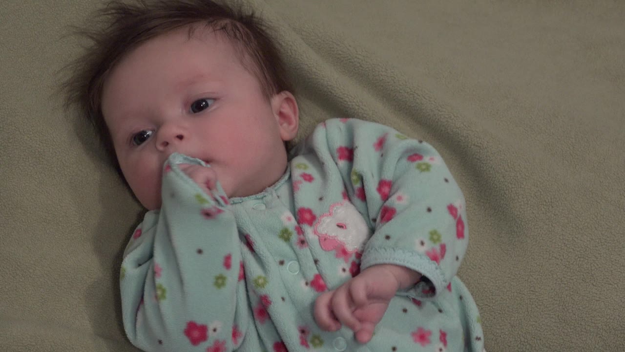 Baby with sleeve partly in mouth while lying on a blanket.