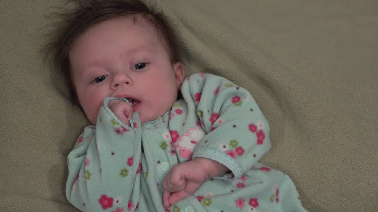 Infant in a pale blue sleeper lying on a green blanket.