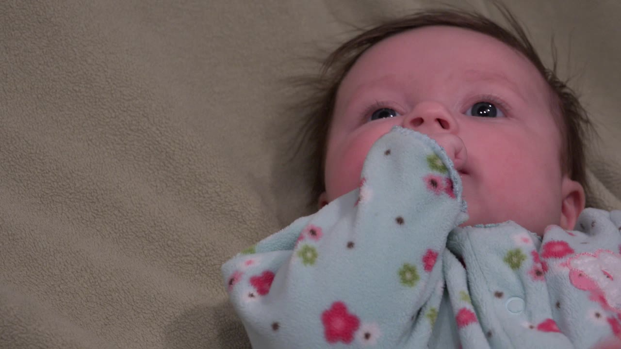 The baby's floral sleeve covers more of the lower face while the child lies still on the beige bed surface in Westminster, Colorado.