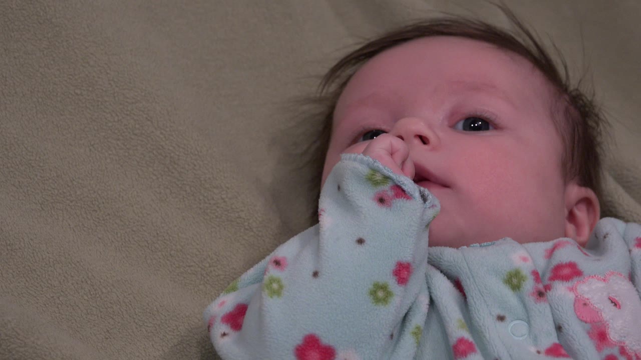 A Westminster, Colorado baby looks upward while the pale blue sleeve covers most of one hand at the mouth.