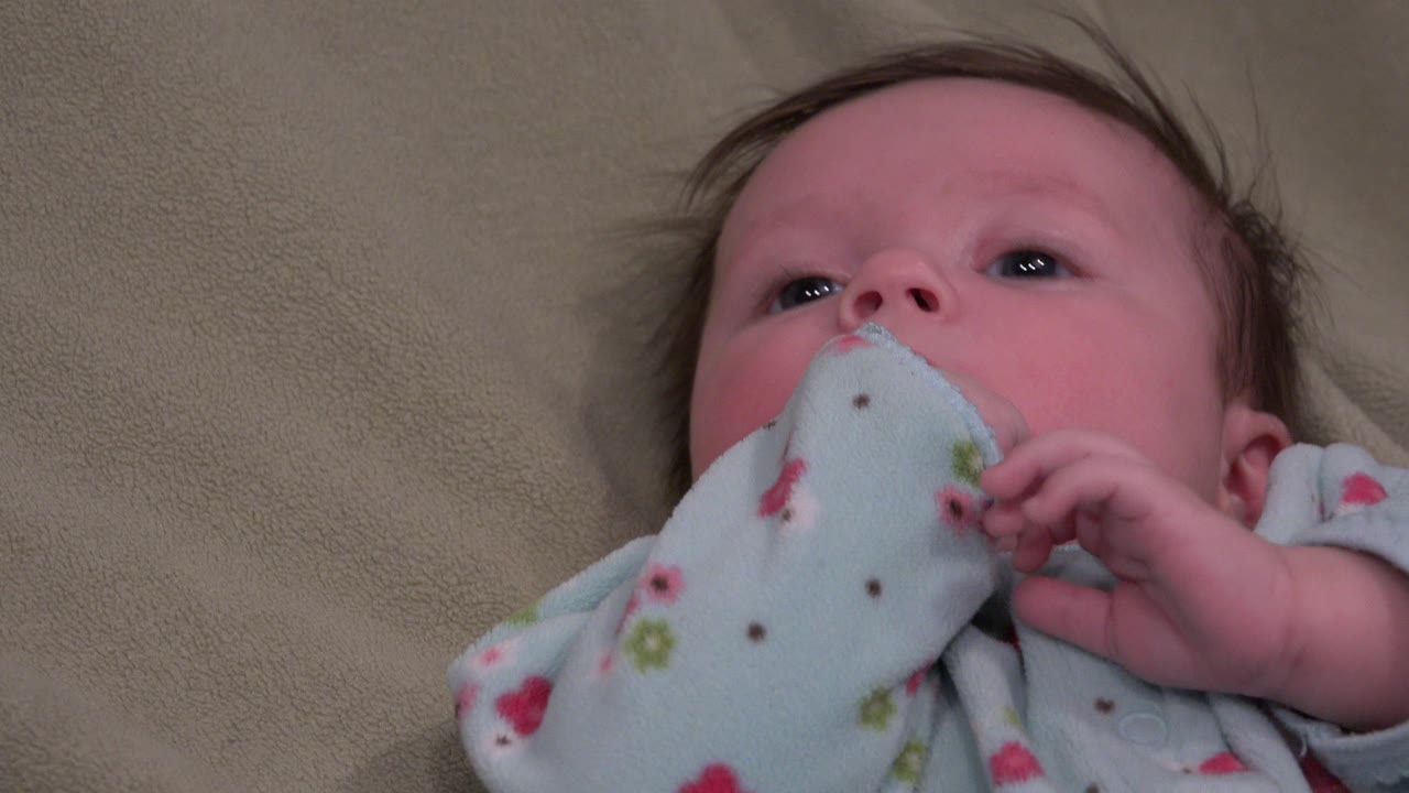 Baby lying on tan bedding with fabric near the mouth.