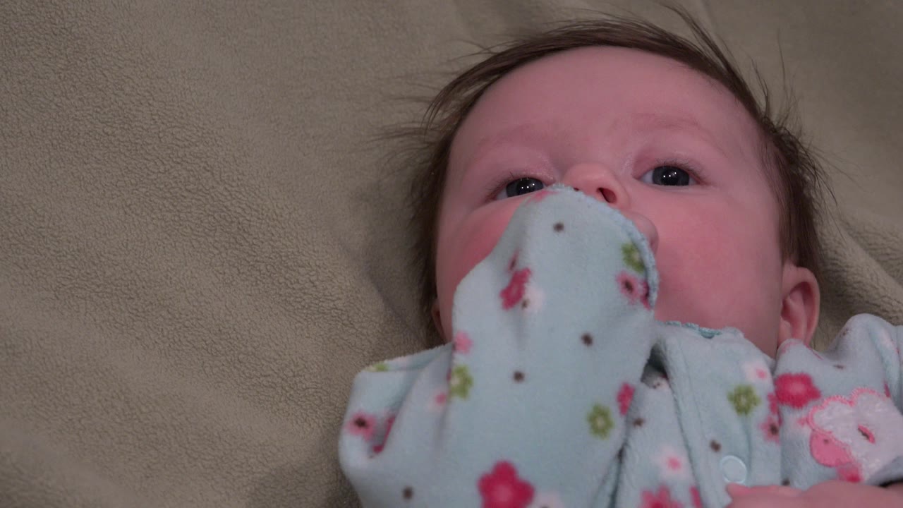 Baby lying on a tan surface with a floral blanket near the mouth.