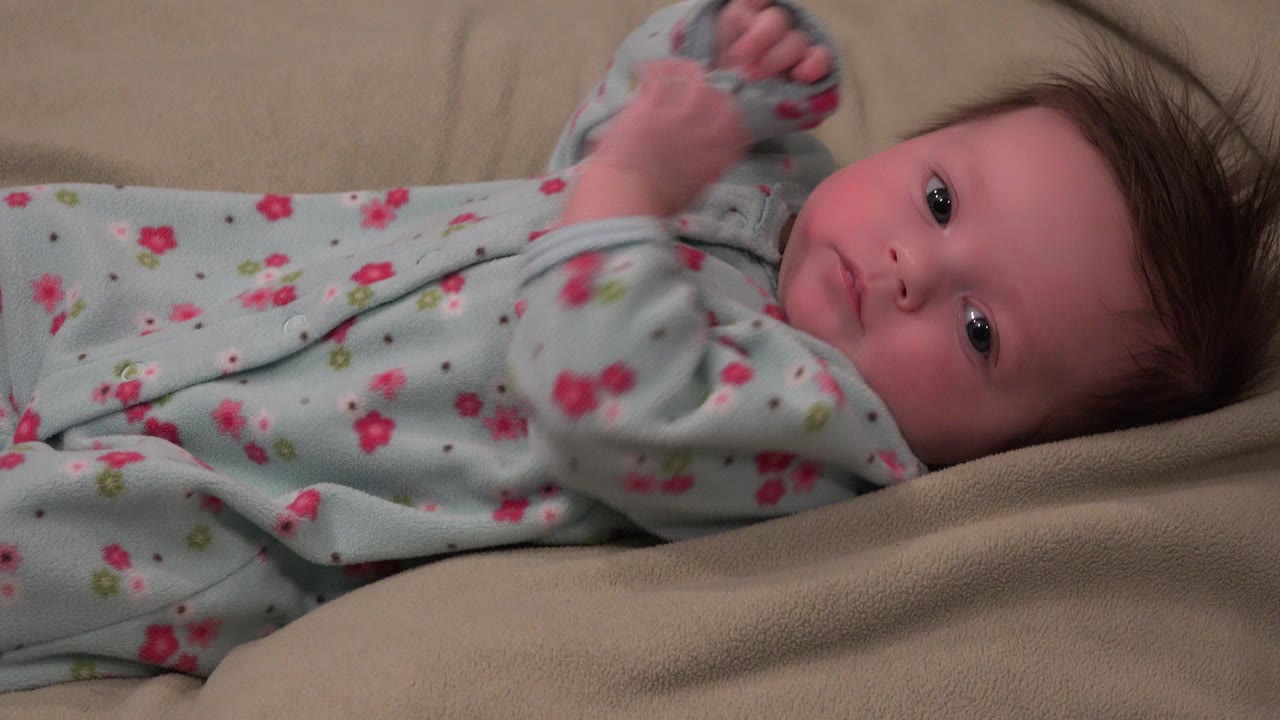 Infant lying on tan blankets in a floral sleeper.