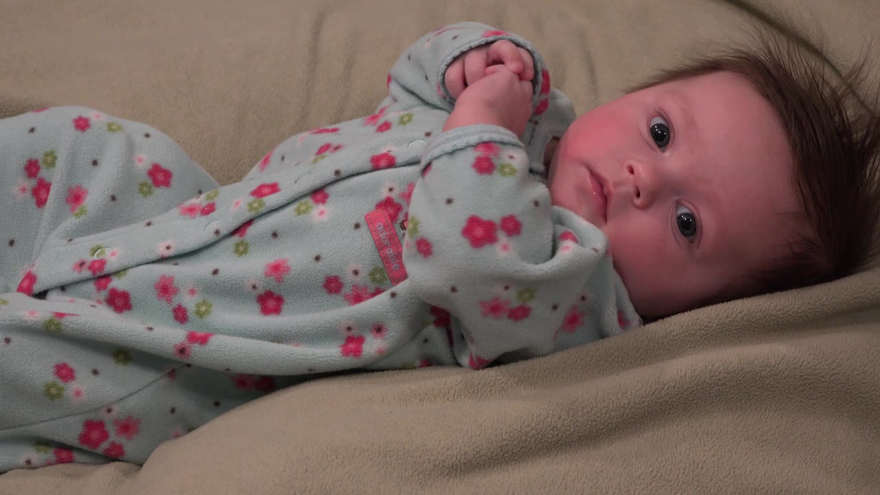 Infant looking outward while lying on beige cushion.