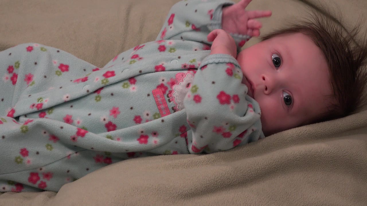 In Westminster, Colorado, the baby keeps looking toward the camera while one arm lifts above the body and the floral sleeper spreads across the beige fabric.