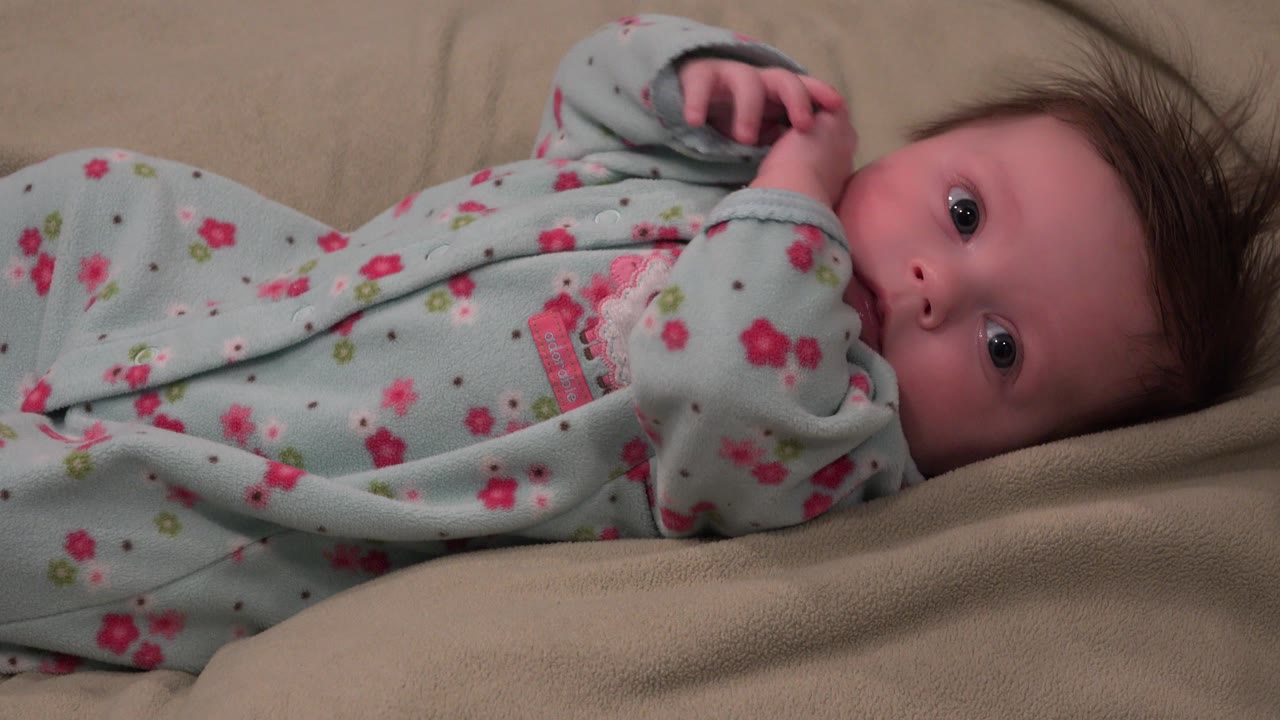 In Westminster, Colorado, the baby lies diagonally across the beige blanket, with both hands closer together near the chest and wide eyes facing the lens.