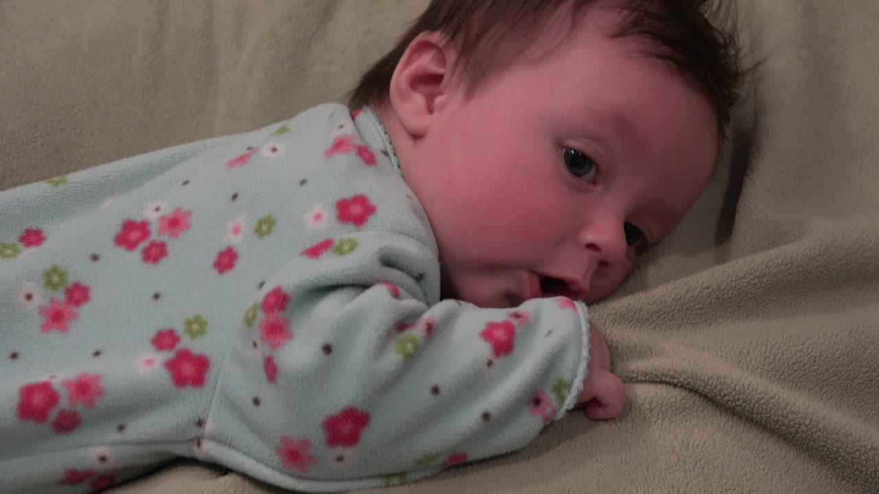 Baby lying face down on a tan couch in a flowered outfit.