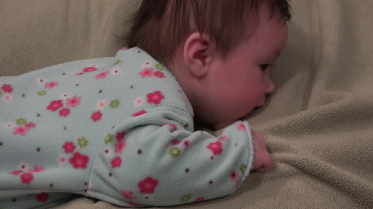 Baby girl remains on her stomach on the beige blanket in Westminster, Colorado, with her face close to the fabric and one arm tucked beneath her shoulder.