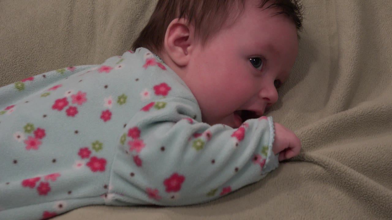 Baby lying on beige sheets in a floral sleeper.