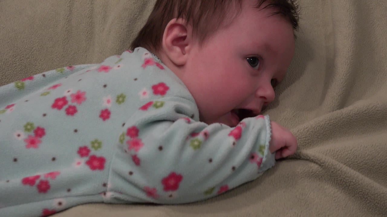The baby remains on the beige sheets in Westminster, Colorado, with the side of the face visible and one sleeve-covered arm pressed into the bedding.
