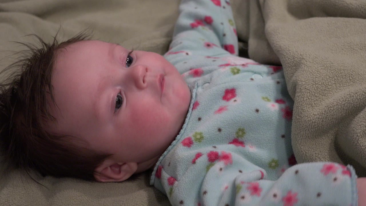 Newborn lying on a beige blanket in blue floral pajamas.