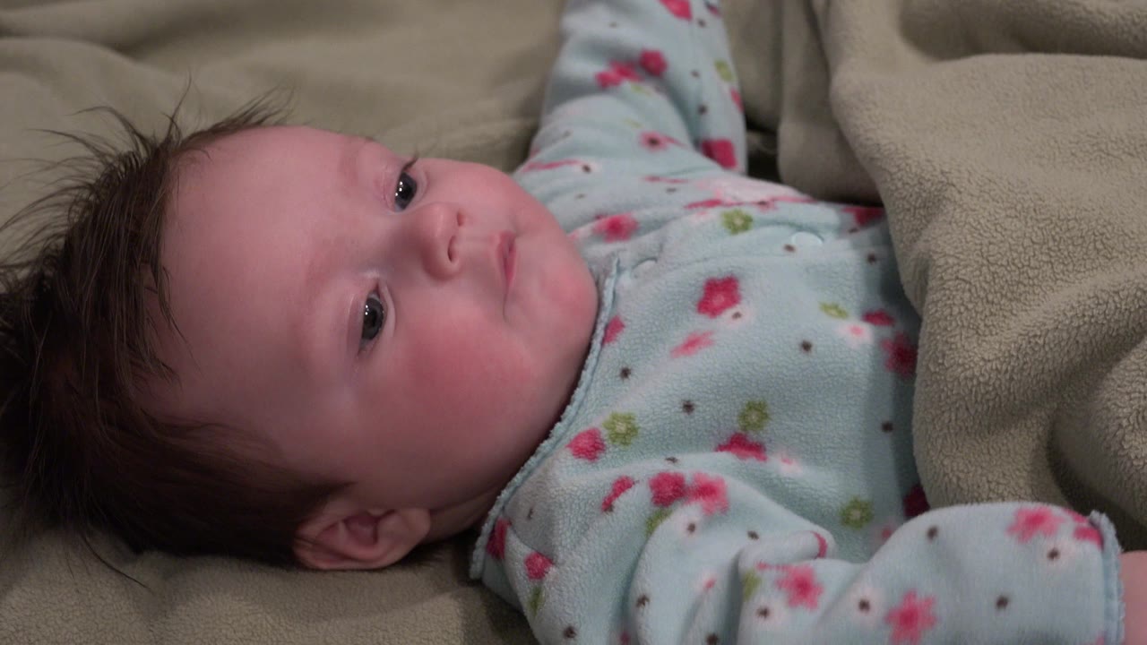 Close-up of the newborn's face on a beige blanket in Westminster, Colorado, with dark hair spread against the fabric and eyes open.