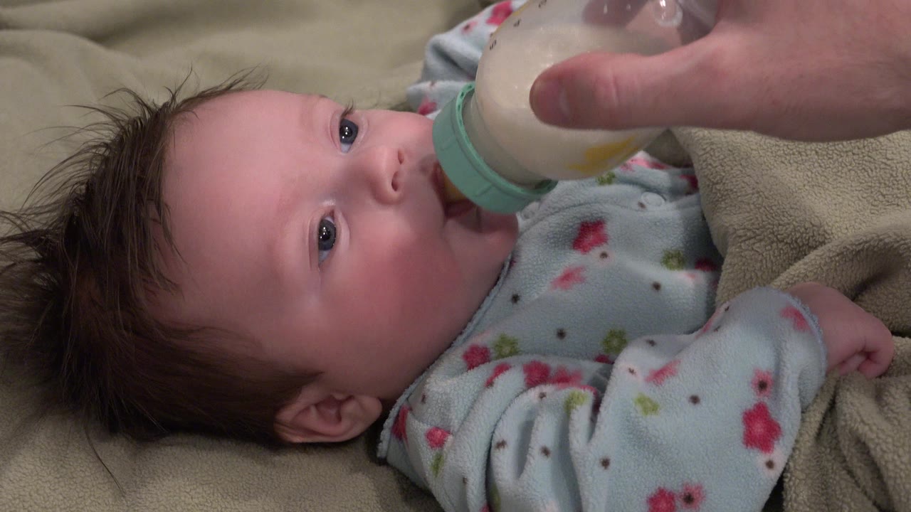 Baby lying down while drinking from a bottle held by an adult hand.