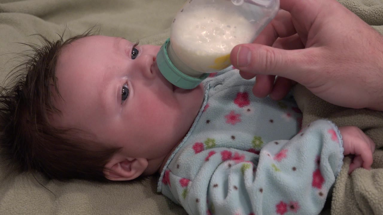 Adult hand holding a bottle as a baby drinks milk.