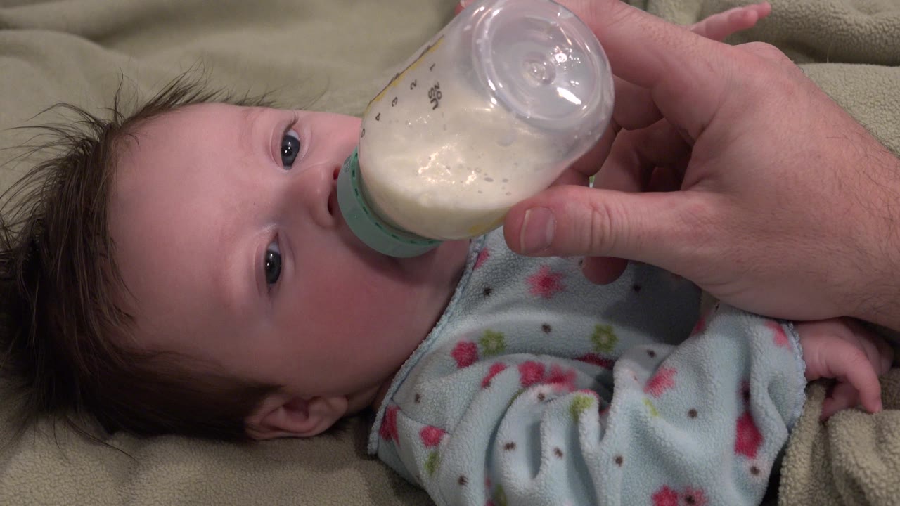 Adult hand holding bottle to baby's mouth.