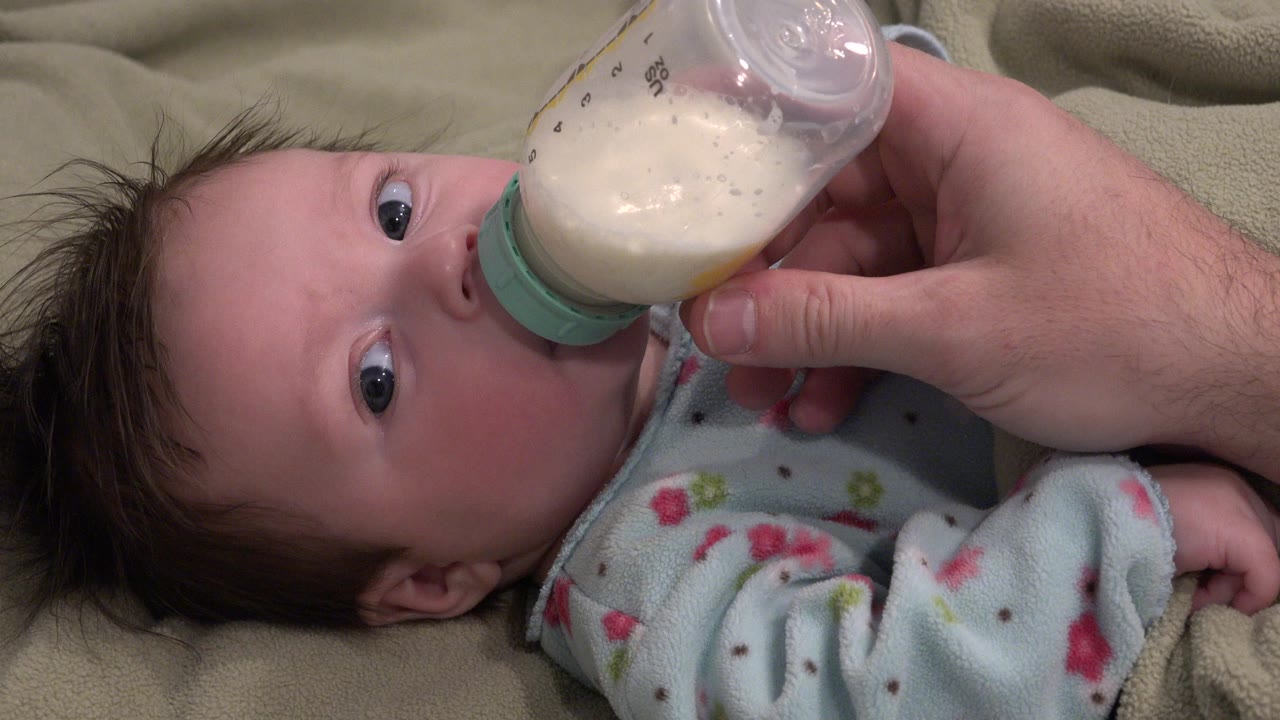 Baby lying on a blanket drinking from a bottle held by an adult hand.
